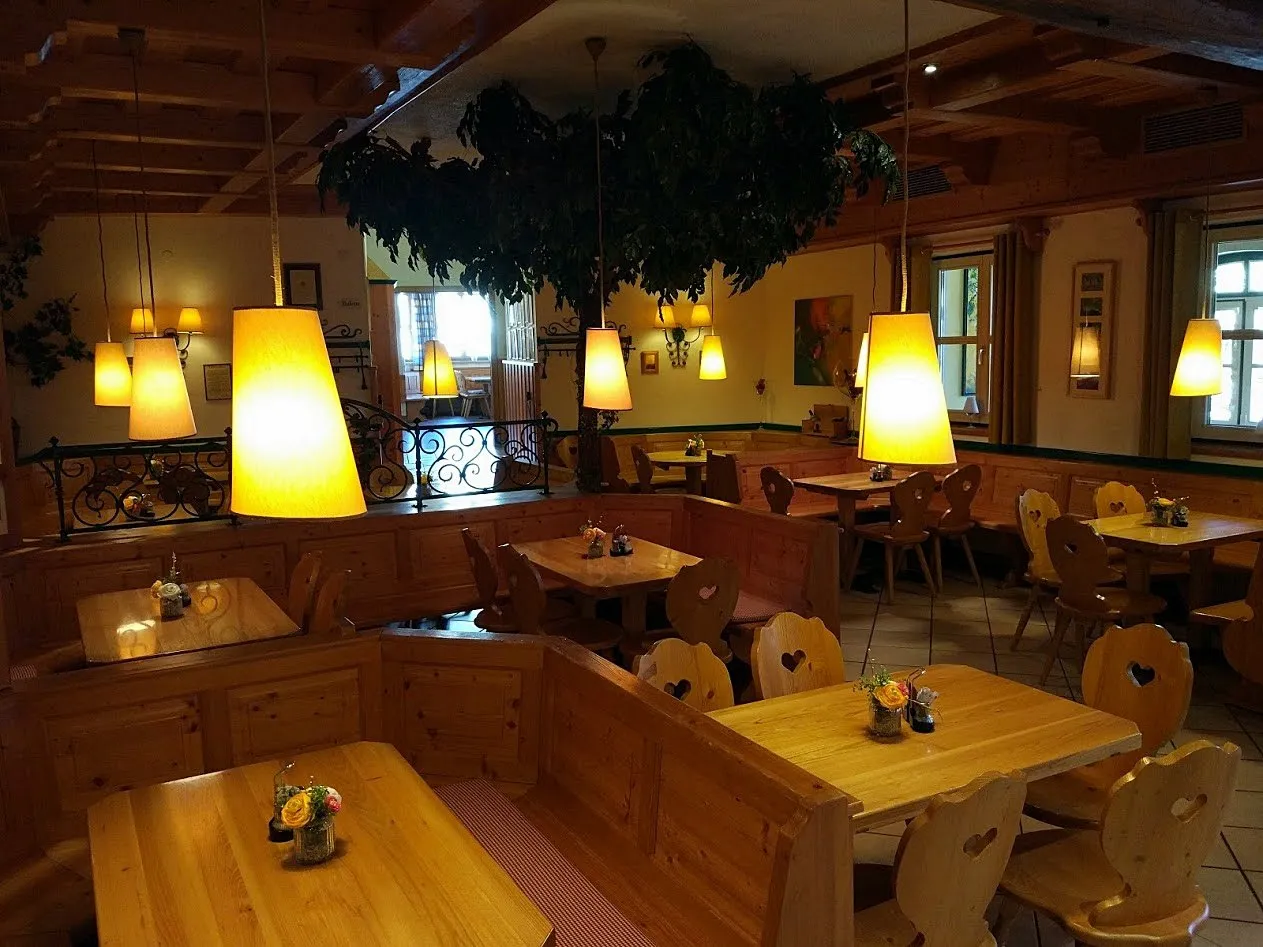 Holzvertäfelte Heurigenstube mit Herzerlstühlen, Holztischen, warmen Lampen und Föhrenzweig an der Decke